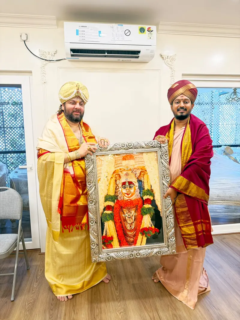 Two men in ceremonial attire holding a framed image of a deity