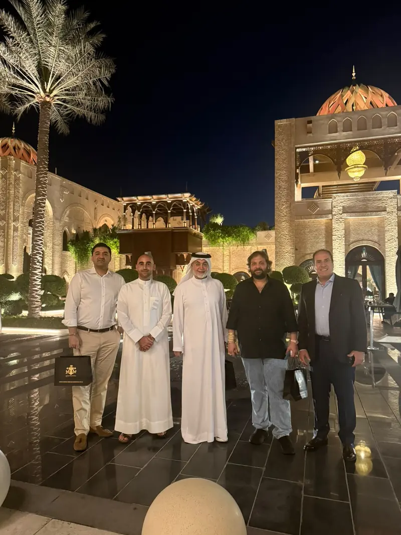 A group in Emirati dress and suits outside an illuminated building at night