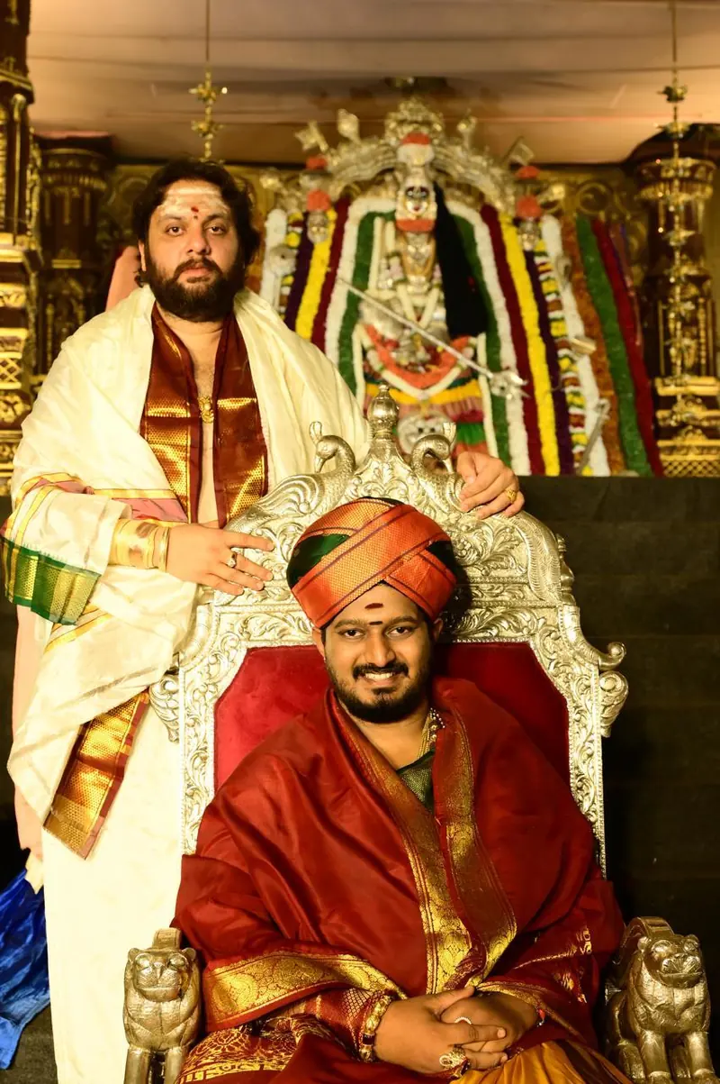 Two men seated before a decorated deity in a temple
