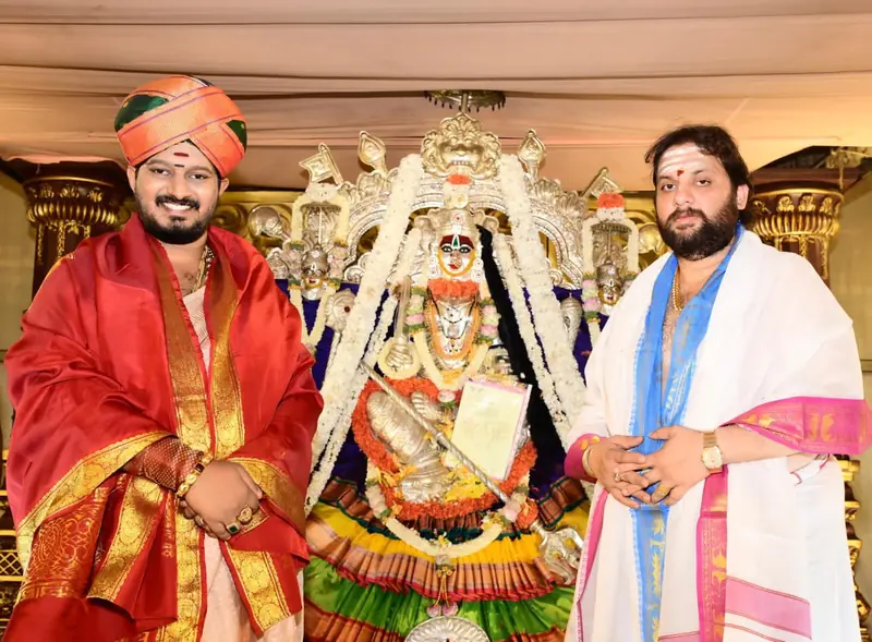 Two men standing beside a decorated deity during a ceremony